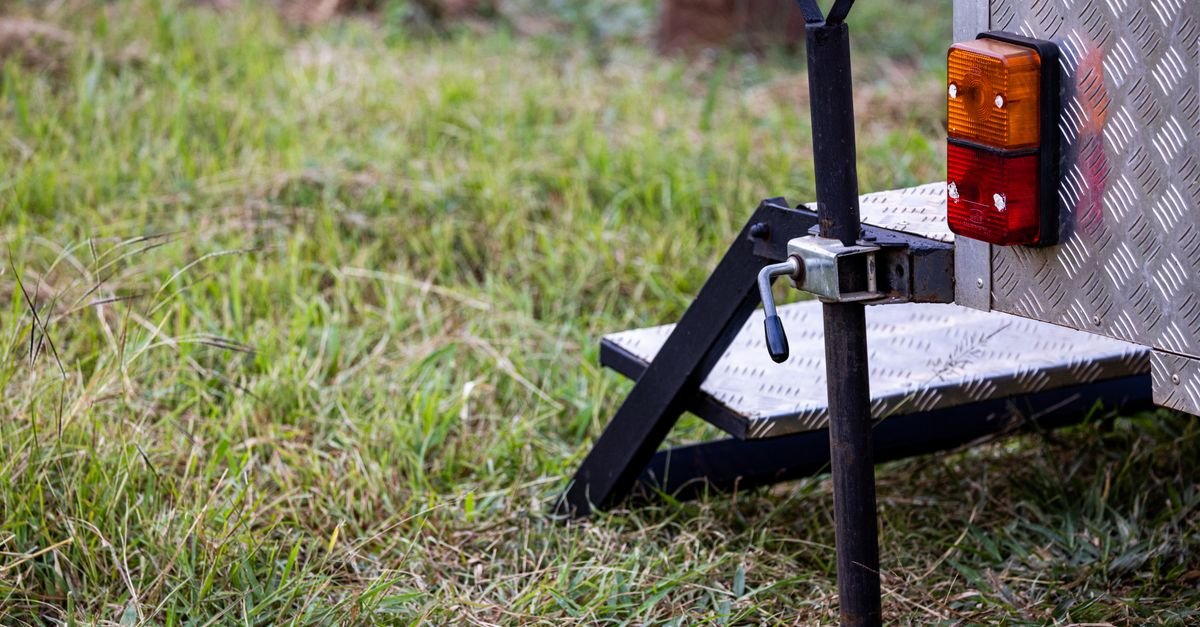 Close-up of a trailer hitch, jack and steps on a camper parked on grass