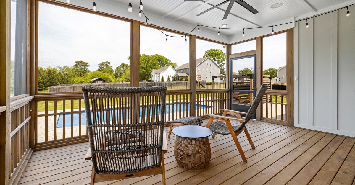 Screened terrace with wooden furniture and a ceiling fan, looking out through the mesh to a backyard