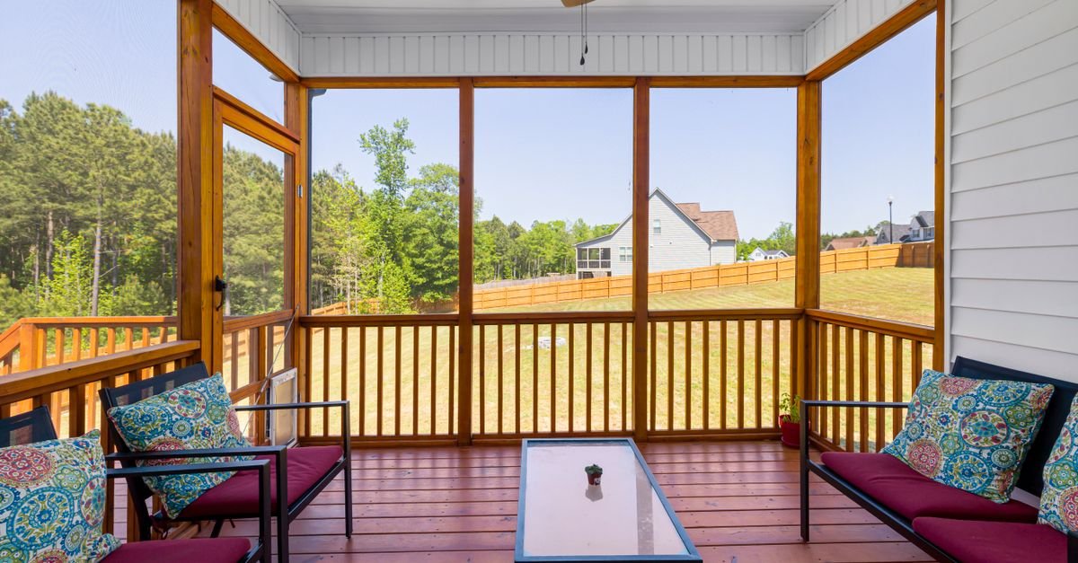 Enclosed screened porch with cushioned furniture looking out to dense green planting