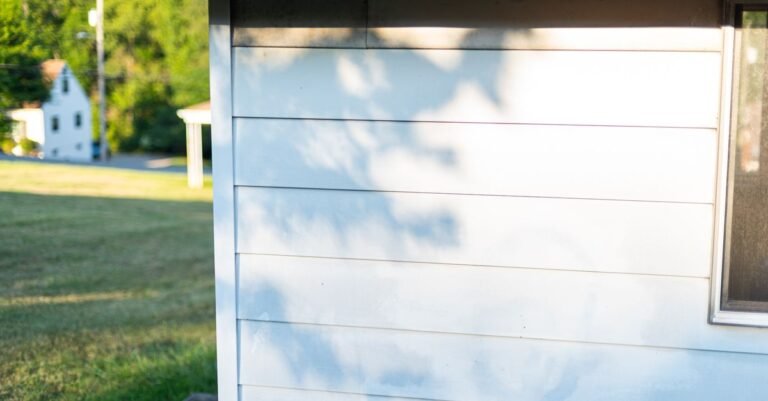 Sunlit siding on the side wall of a house with tree shadows falling across the boards