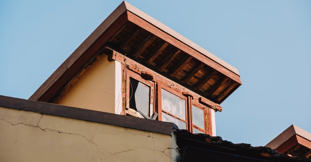 A dormer with an open eave, exposed rafter ends and a weathered painted timber fascia board along the roof edge
