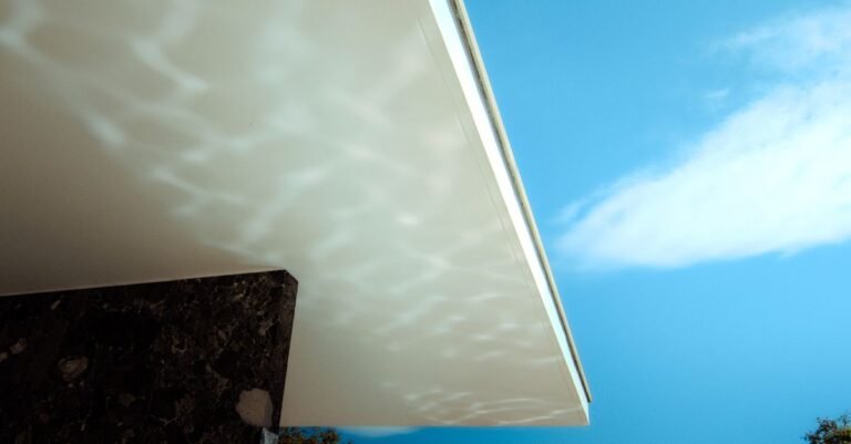 The underside of a deep white roof overhang seen from directly below against a blue sky
