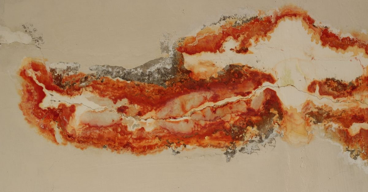 Orange and red rust staining spreading across a masonry wall surface