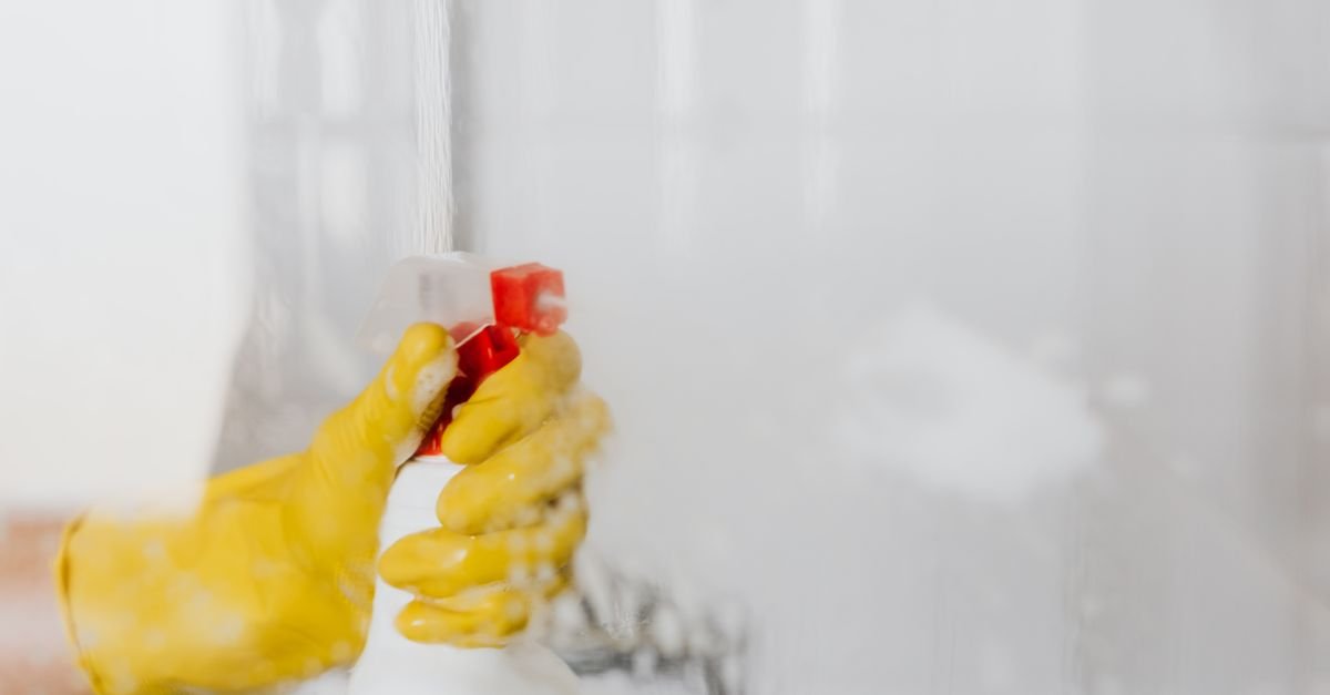 Gloved hand spraying cleaning solution onto a surface before scrubbing