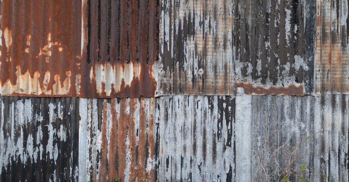 A rusting corrugated metal wall with paint peeling back from the corrosion beneath it