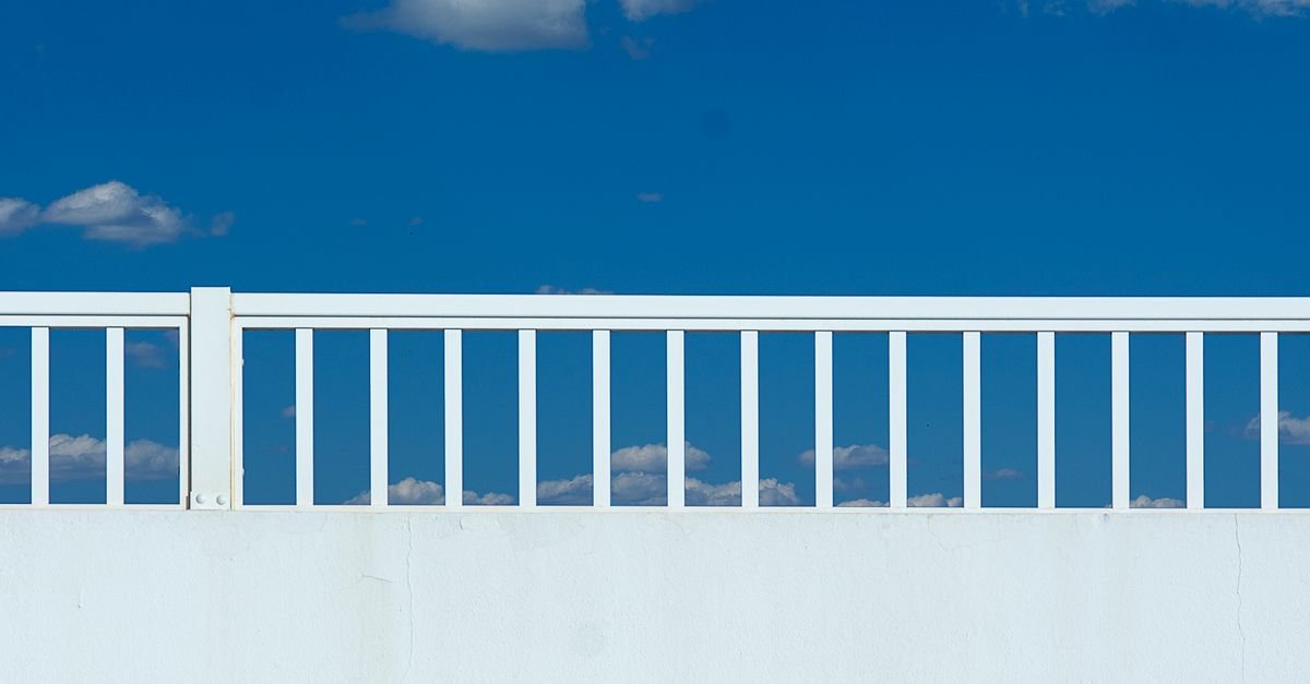 White fence balusters above a rendered wall with orange bleed running from a bolted post fixing