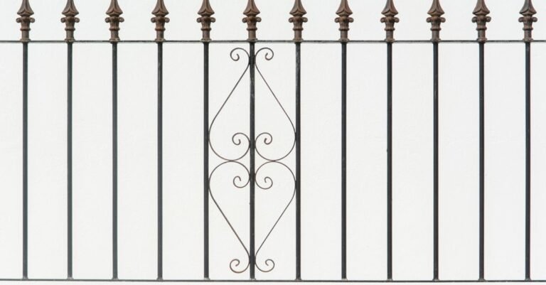 Ornate black wrought iron fence with symmetrical scrollwork and pointed finials in sound condition