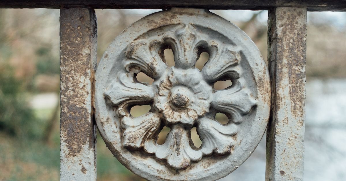 Close-up of ornate iron railings with a floral pattern where rust has broken out through the old finish