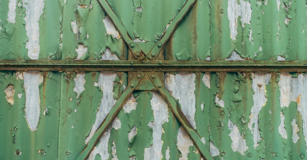 Close-up of a green metal gate where peeling paint has failed and rust has taken hold underneath