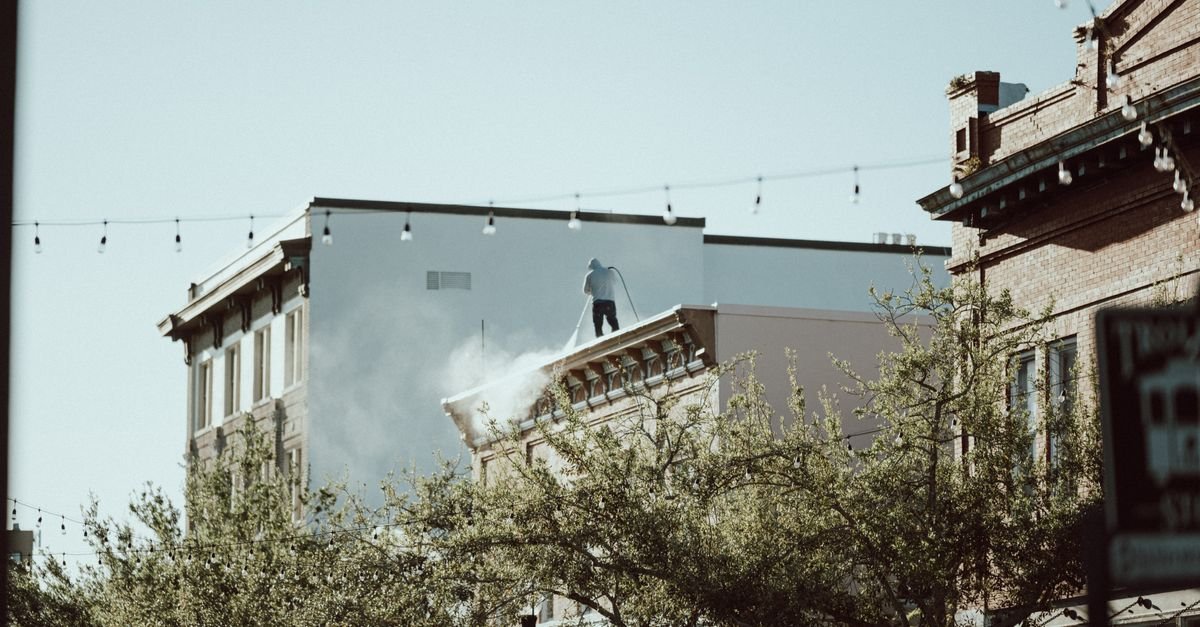Contractor pressure washing the parapet of a commercial building from its rooftop
