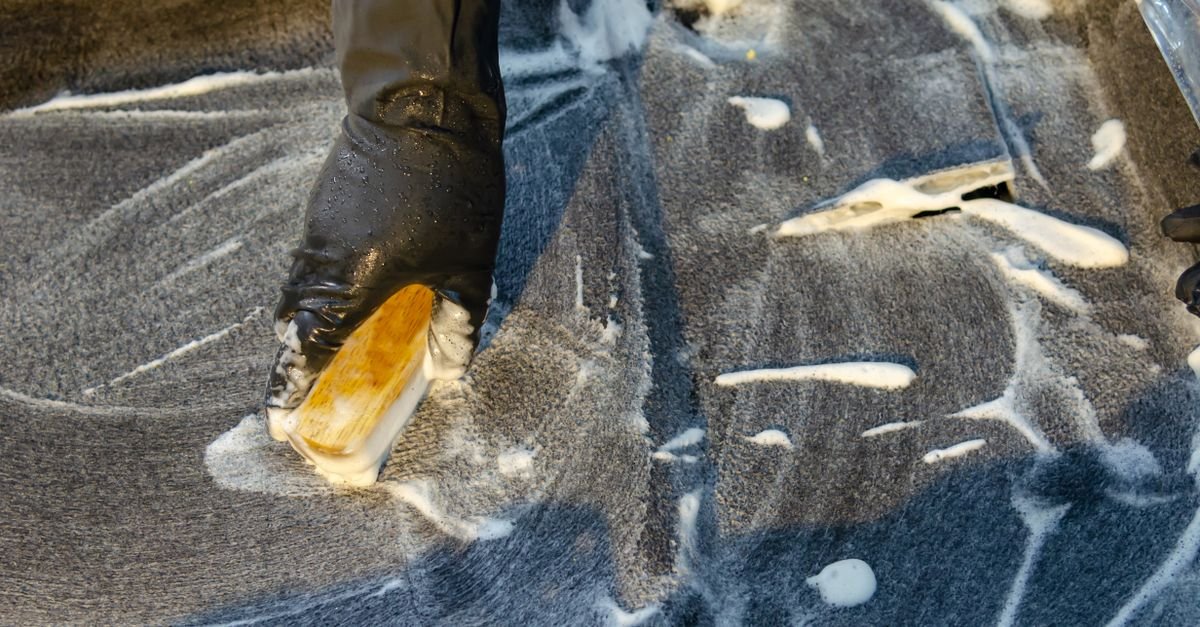 Gloved hand working detergent into a surface with a soft-bristle brush, the method composite tile makers publish