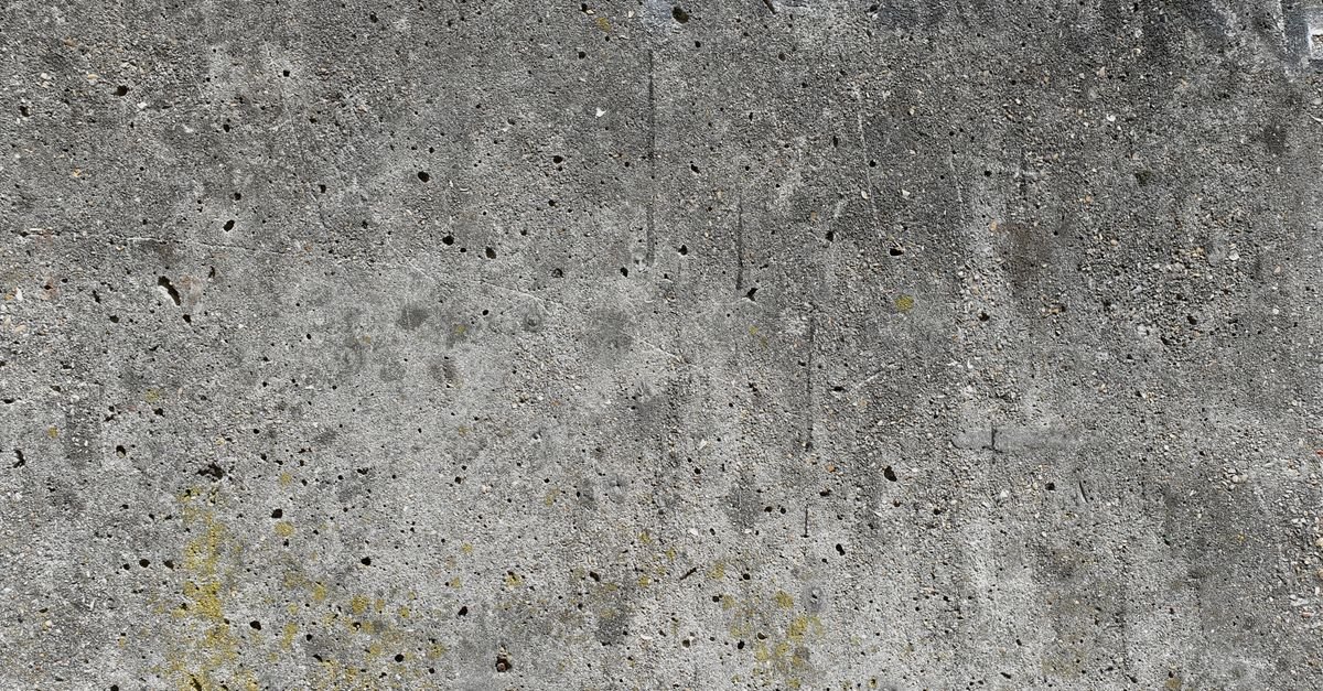 Weathered concrete surface showing dark staining and open pores in the cement paste