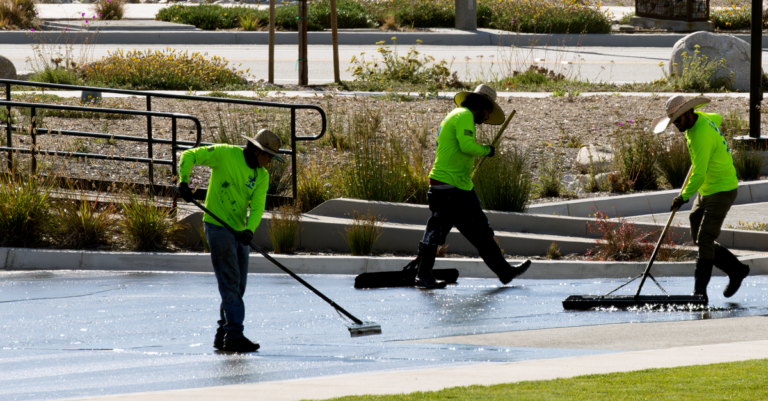 Cleaning crew in bright uniforms working across a paved concrete walkway in sunlight