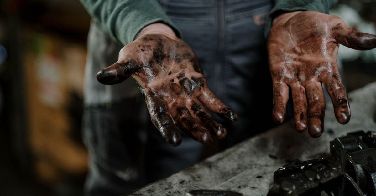 Grease and oil coating a mechanic's hands in a workshop, the same carbon-chain soil that soaks into a concrete floor