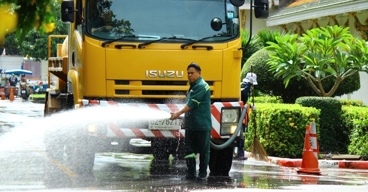 A worker operating a high-volume water hose from a municipal street-cleaning truck