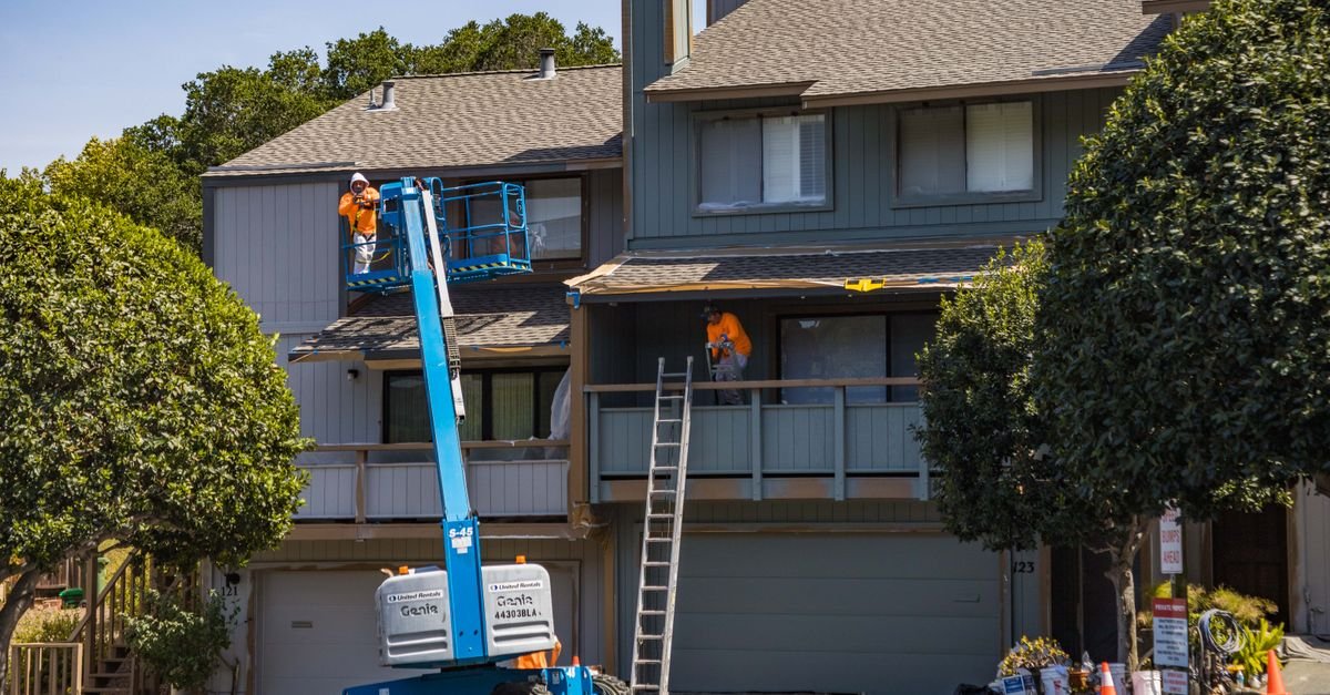 Workers on a hydraulic lift platform working at height on a house exterior
