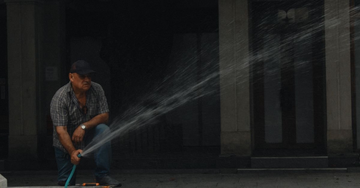 A man spraying a stone wall with a hose from ground level, both feet planted
