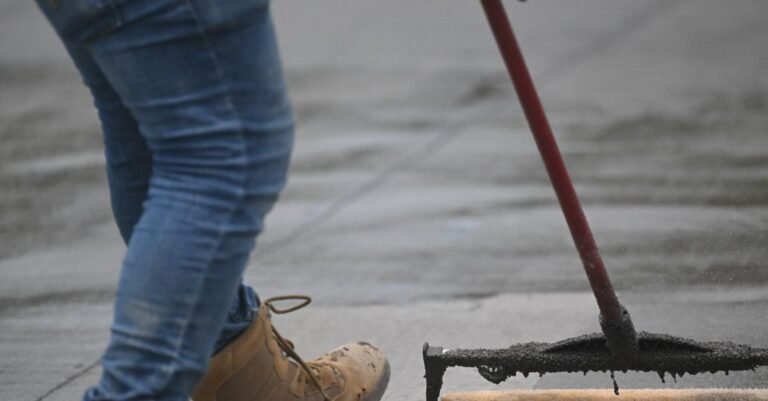 A worker rolling concrete sealer across a clean pavement slab in overlapping passes