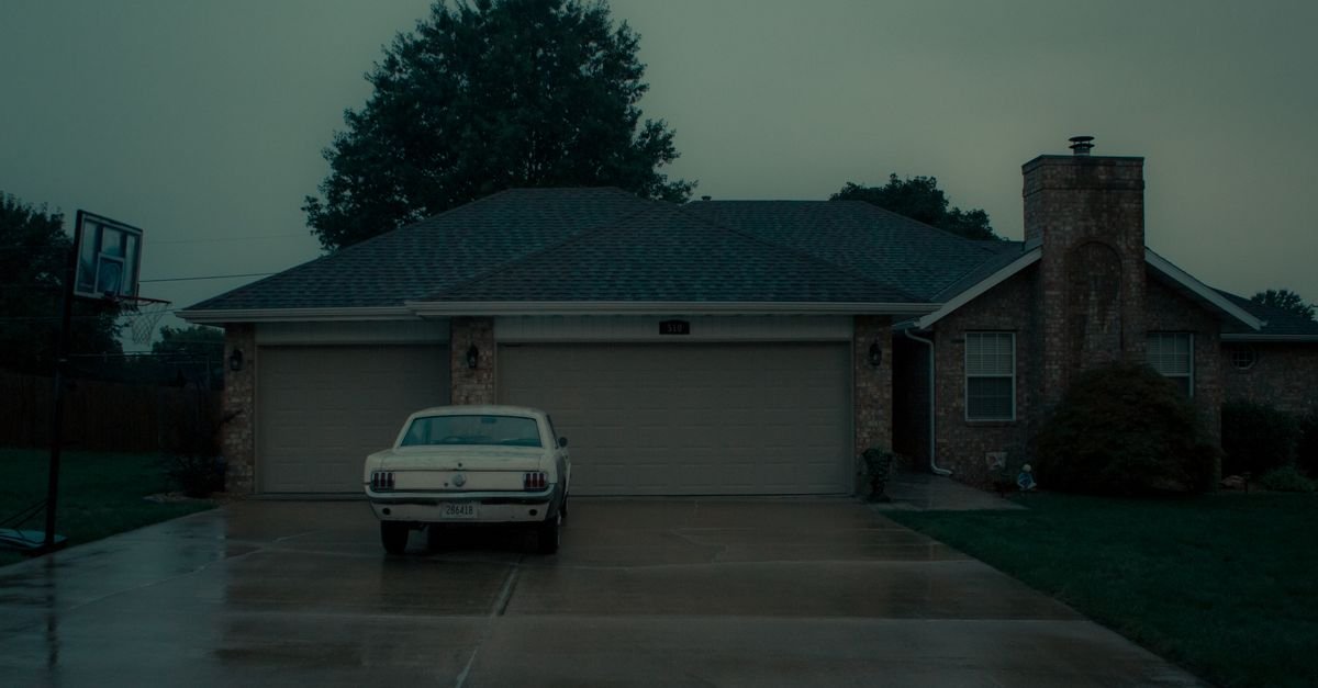 A vintage car parked on a wet suburban driveway on a rainy day, the surface condition no sealer should meet