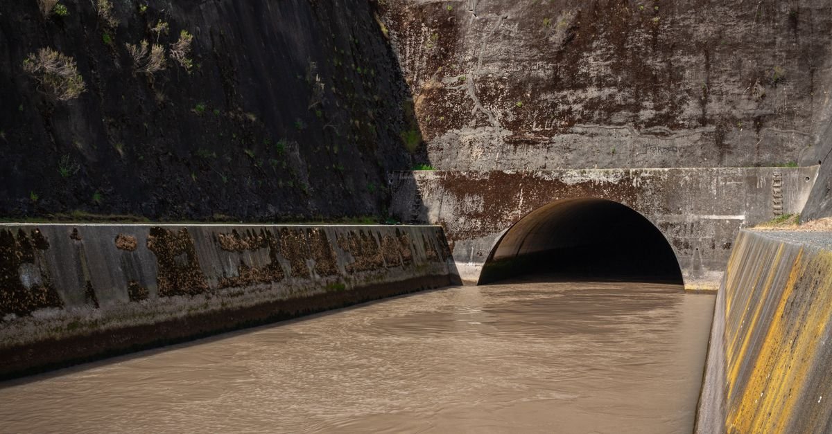 Concrete storm drain outfall with murky water running into a tunnel