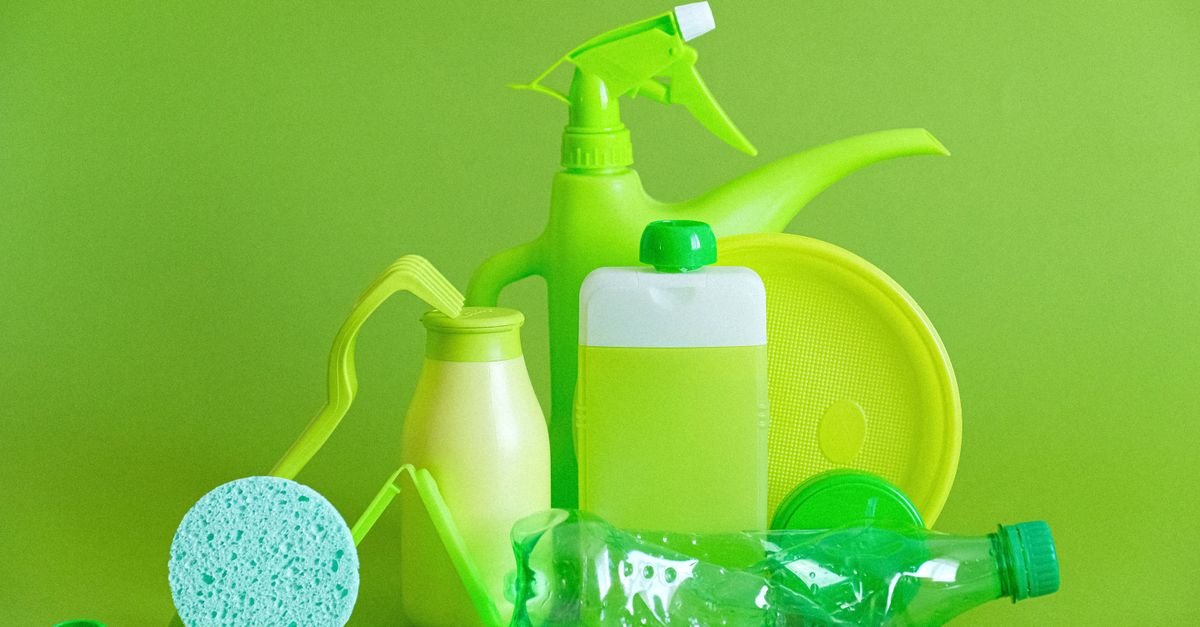 Green plastic bottles and containers of cleaning liquid arranged on a green background