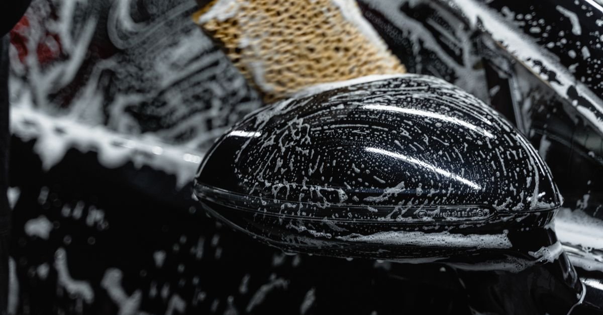 Hand using a soapy wash mitt to scrub a car's side mirror during contact washing