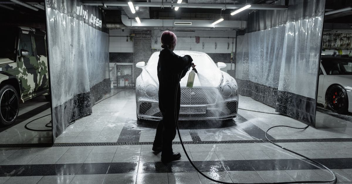 Person applying foam to a car with a wand in an indoor detailing bay