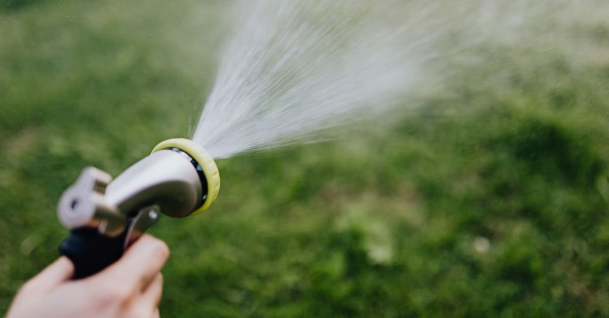 Hand using a garden hose sprayer nozzle to water grass, the style of attachment sold as a pressure washer