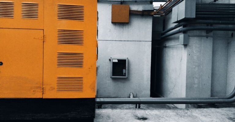 An industrial generator installed outdoors with its piping and wiring exposed against a concrete wall
