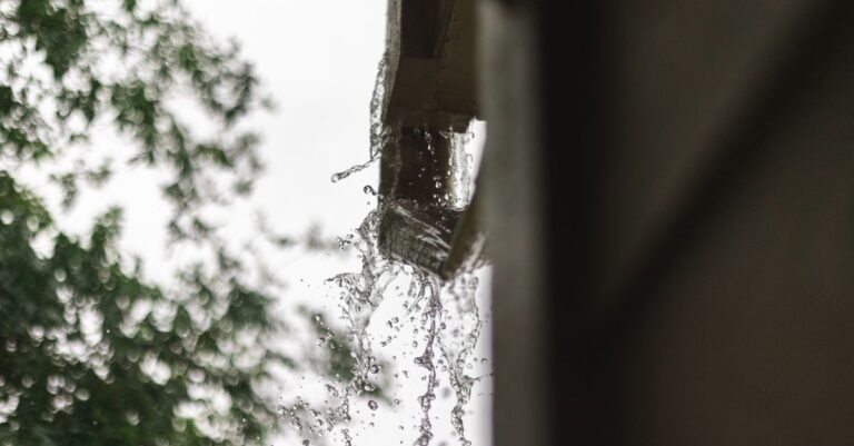 Rainwater pouring over the lip of a blocked gutter instead of running down to the downspout
