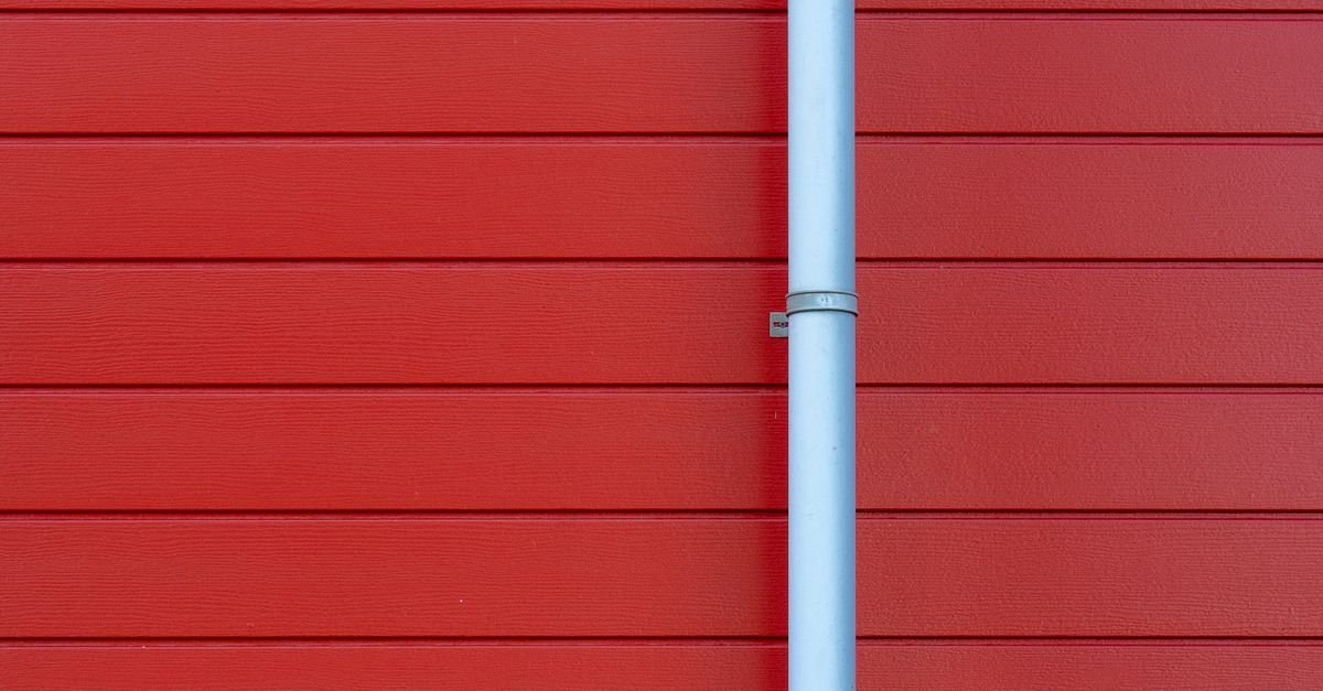 A white aluminium rain gutter mounted against a red wall, showing the bracket line and sealed joint