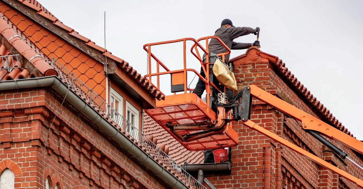 A roofer working at height from a cherry picker on a brick building, keeping both hands free