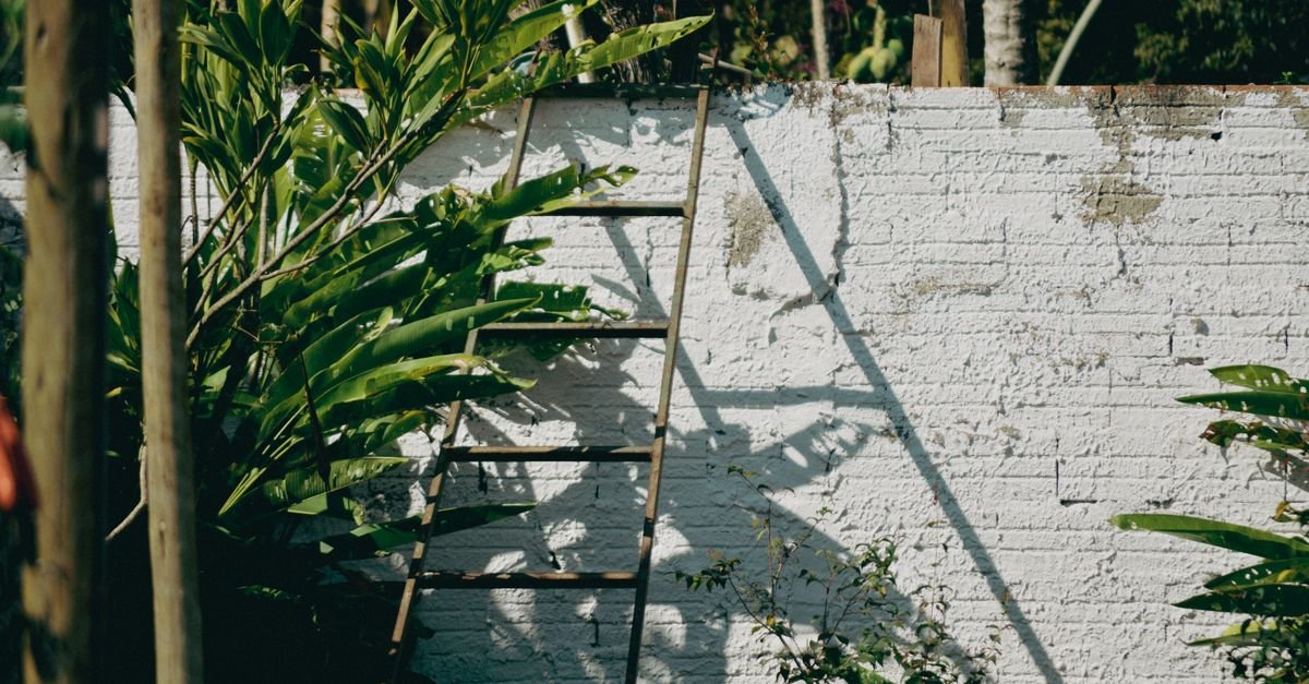 A metal ladder standing on open ground with its feet resting against a brick garden wall