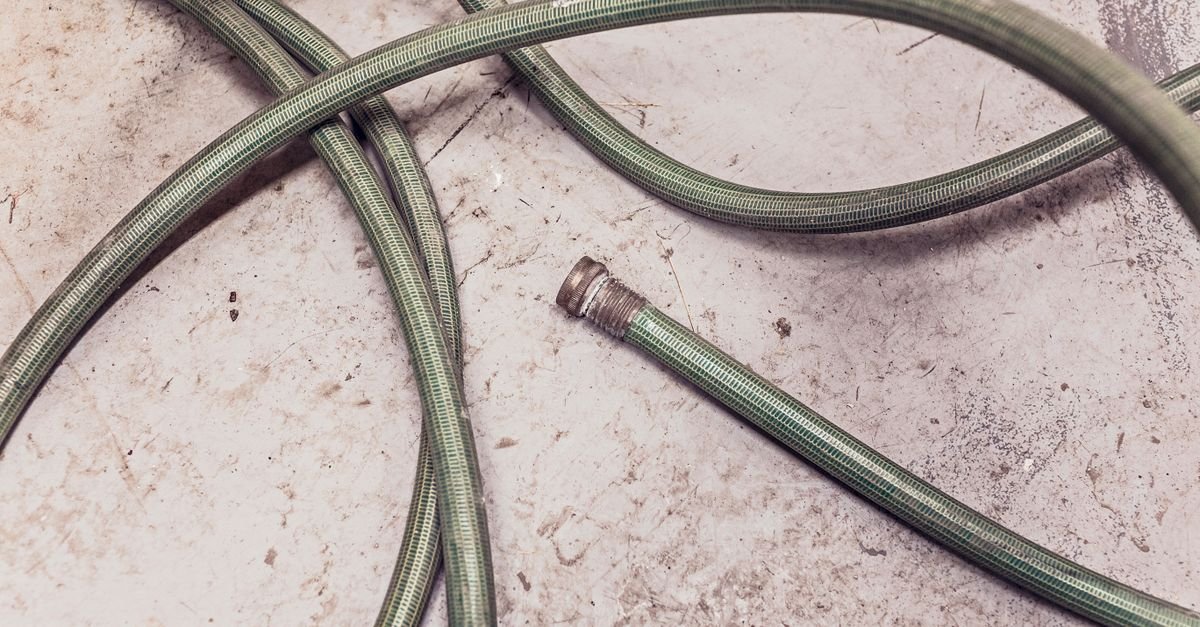 A green garden hose left coiled loose on a concrete slab where it picks up kinks and flat spots