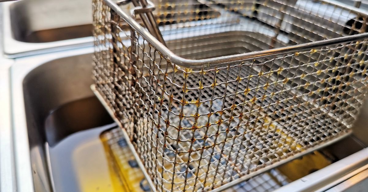 Stainless steel fryer basket sitting above a tank of hot cooking oil in a commercial kitchen
