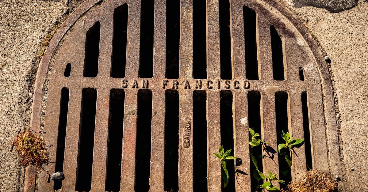 A weathered cast-iron storm drain cover set into a city pavement
