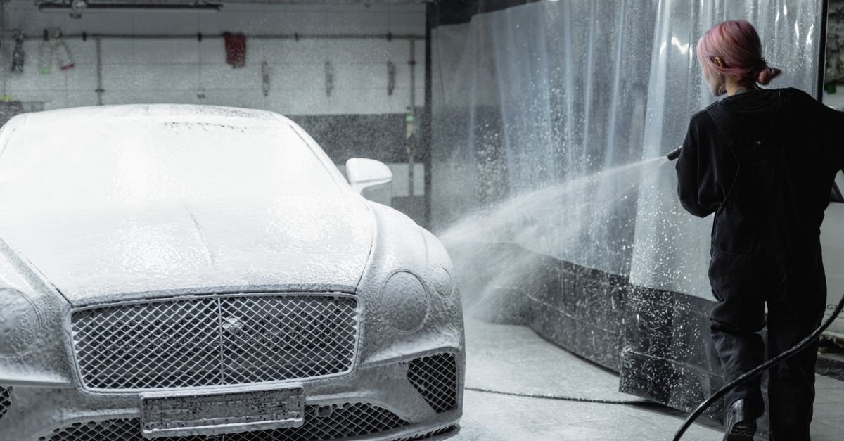 A person holding a pressure washer gun and quick-connect spray tip while cleaning a car in a garage