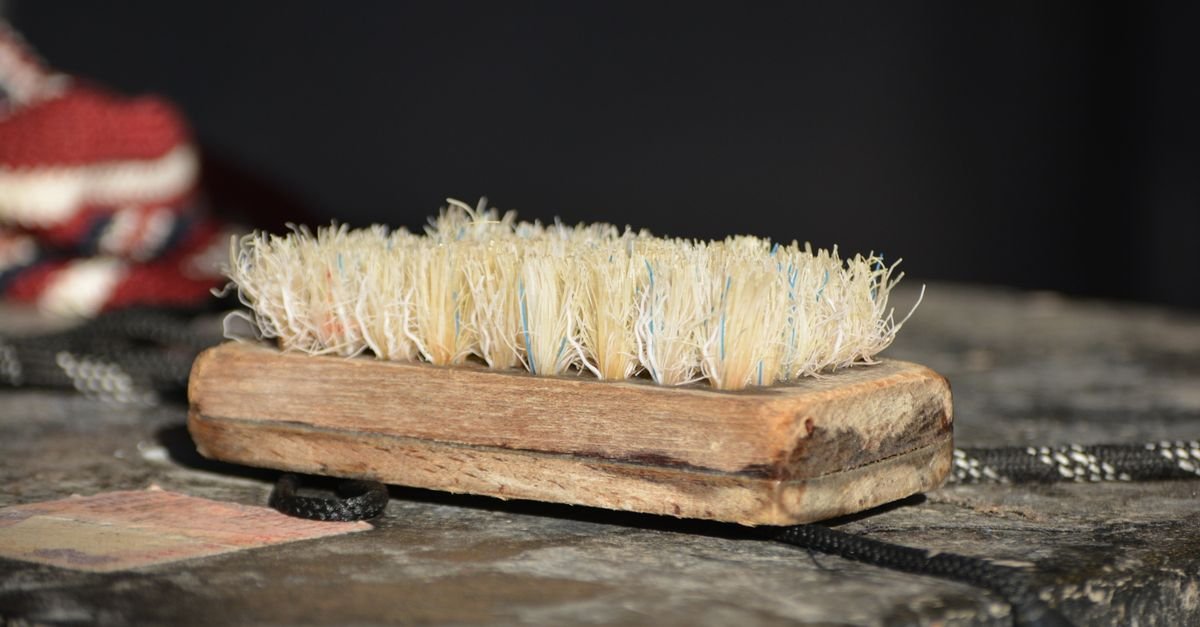 An old wooden-backed scrubbing brush with stiff natural bristles resting on a rough timber surface