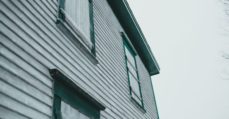 Low-angle view of an older house with weathered painted timber cladding and shutters