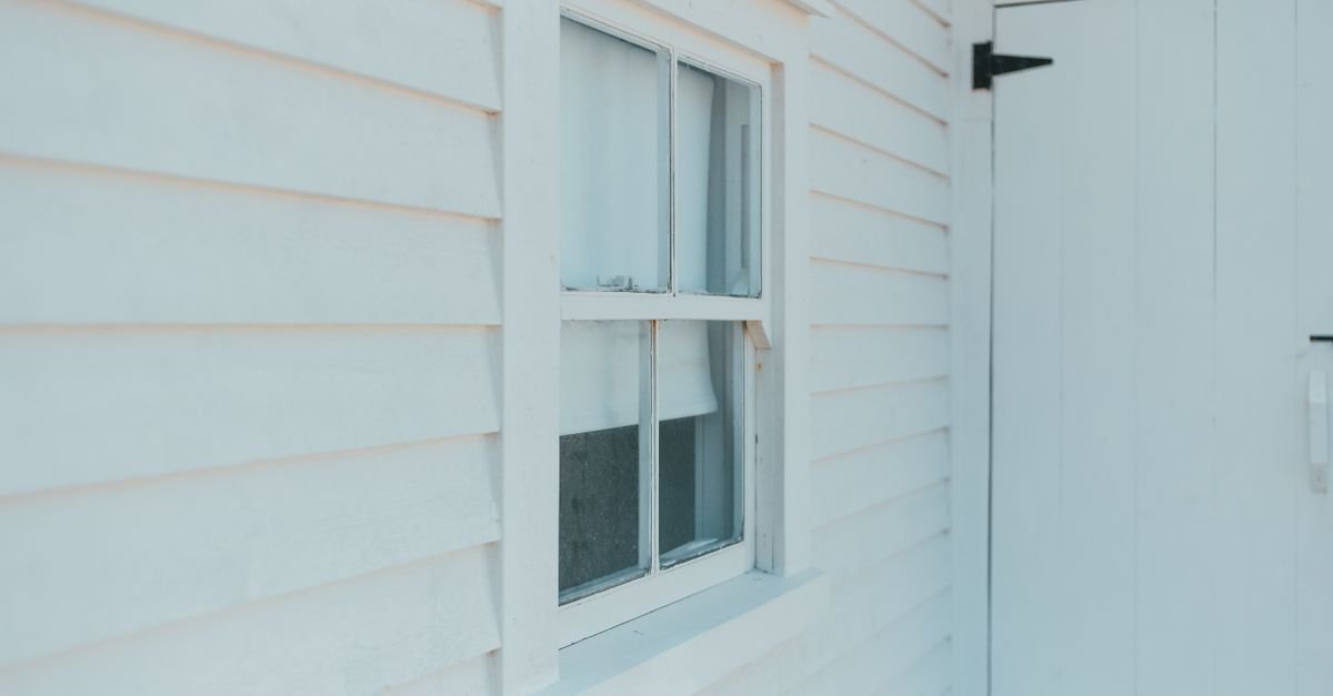 Close-up of a white timber-clad house facade with a window and door, showing the run of the boards