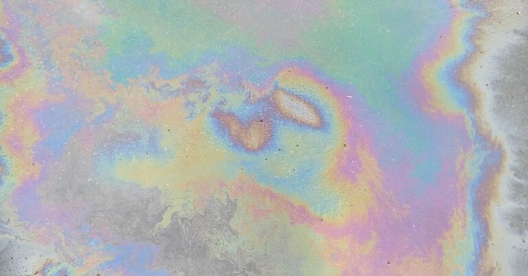 Iridescent oil sheen spreading in coloured bands across a pavement surface