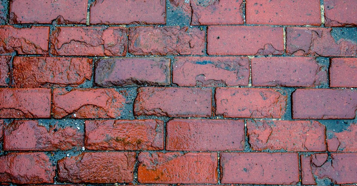 Close-up of a red brick wall soaked with water, the surface dark and running