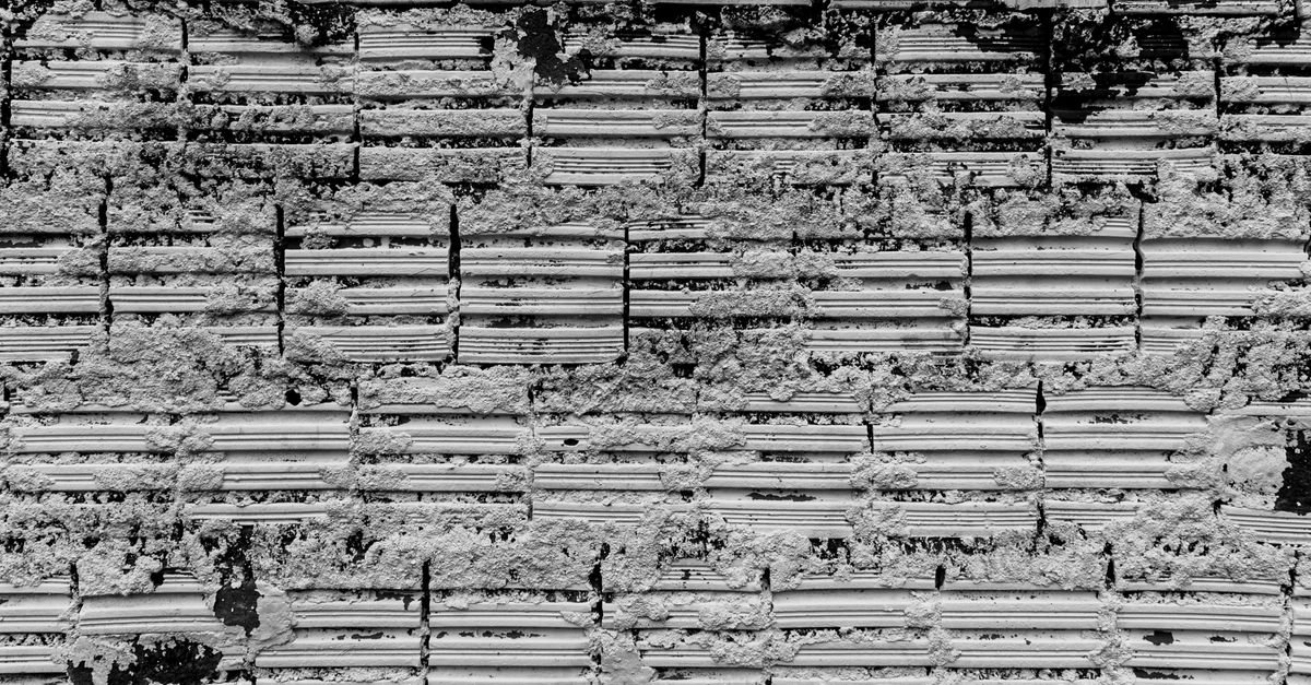 Weathered brick wall with sections of plaster and surface material flaking away from the face