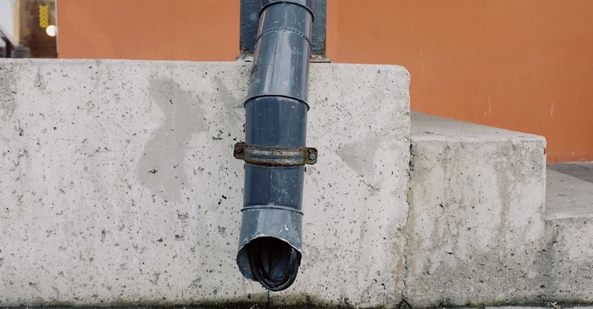 Metal drainpipe running down an aged exterior wall with water staining spreading beneath it