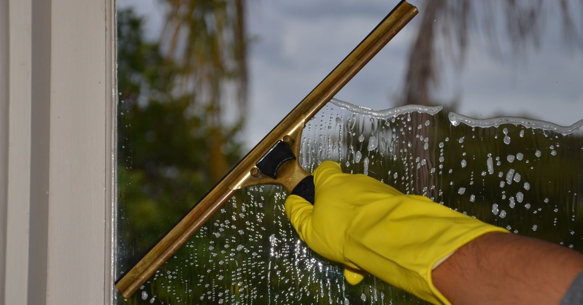 Gloved hand pulling a squeegee down an exterior window pane during cleaning