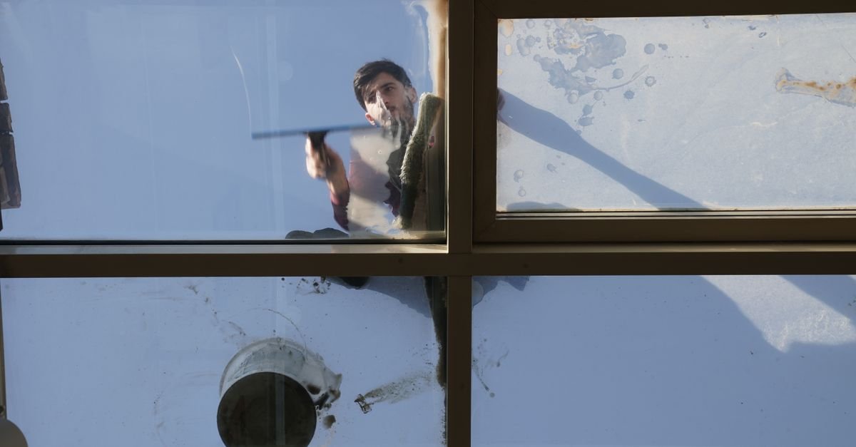 Water running down the outside of a glass roof as a cleaner rinses the panes from above