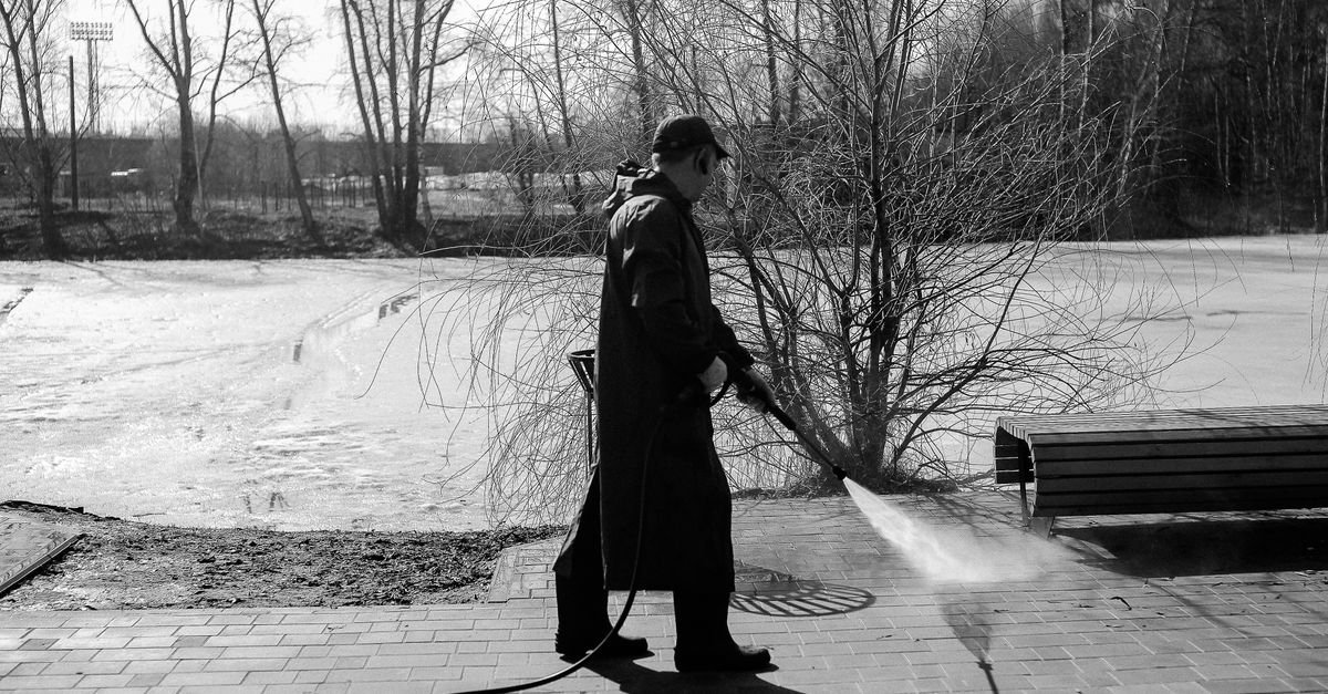 A person pressure washing a paved surface in straight overlapping lanes