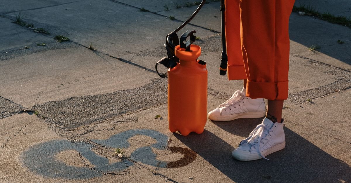 A person in orange work trousers applying cleaning solution to concrete pavement with a sprayer