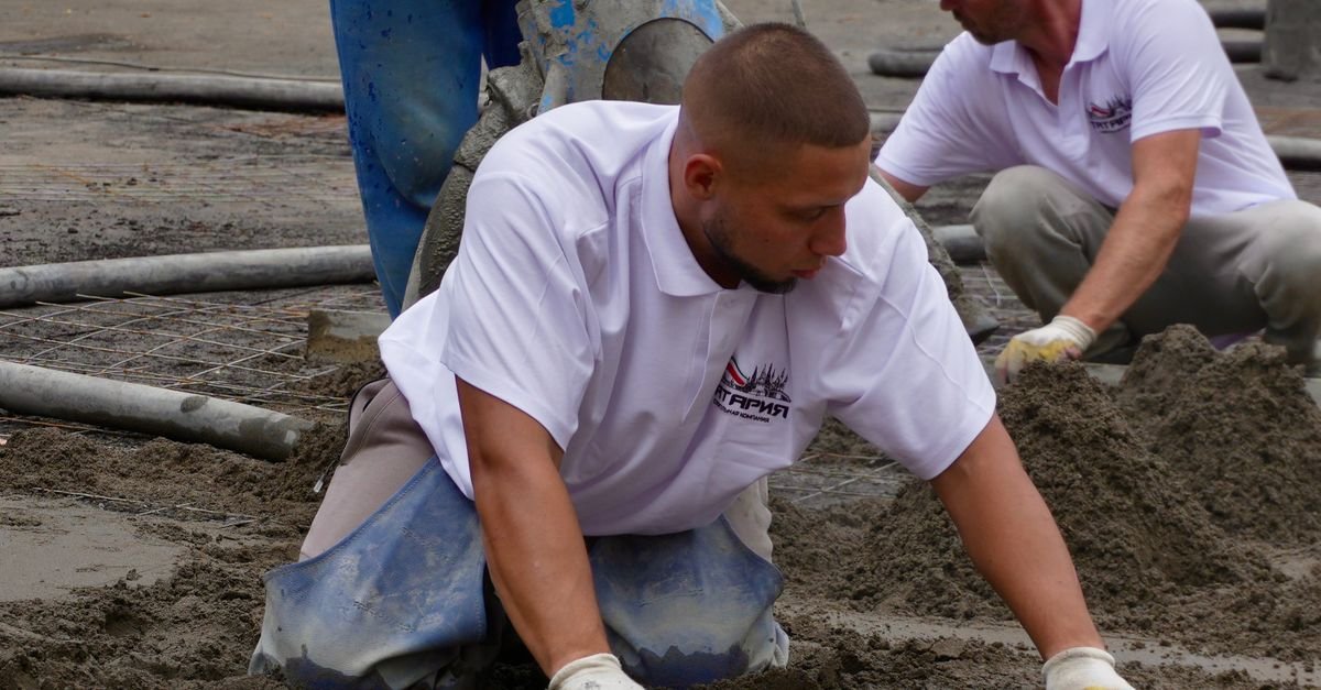 Construction workers levelling a freshly poured concrete slab with hand tools