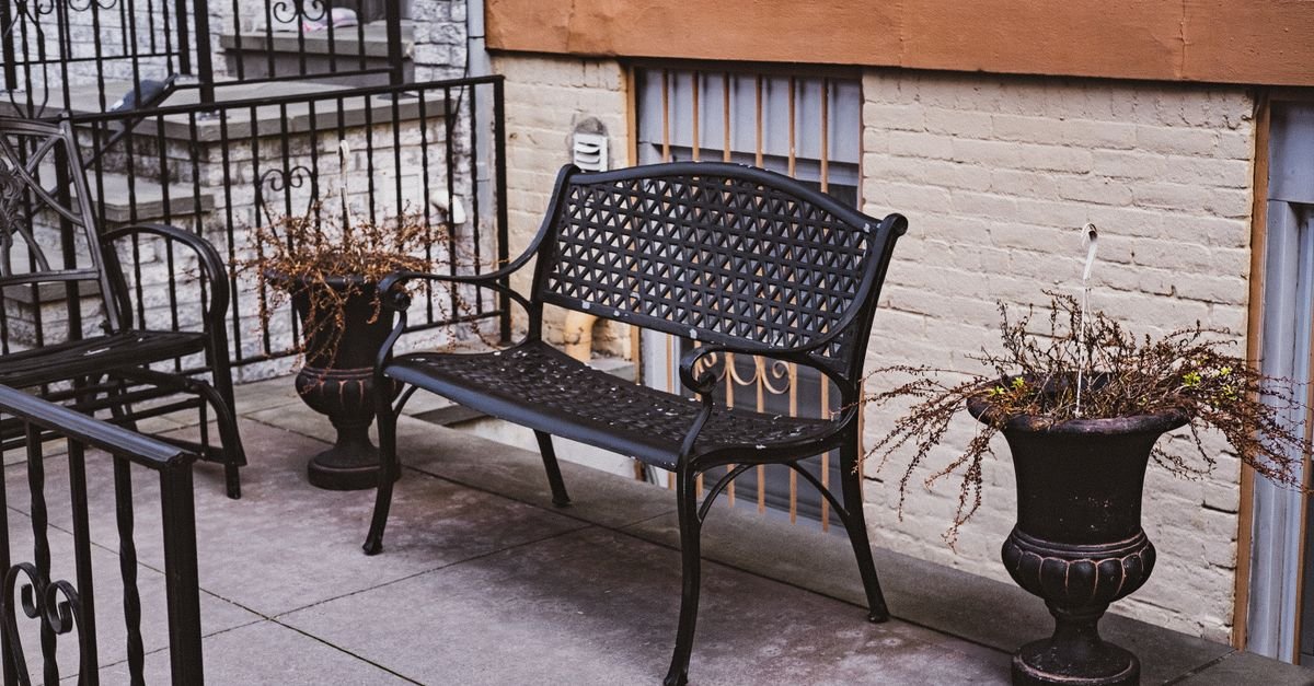Powder-coated metal garden bench beside potted plants on a paved terrace